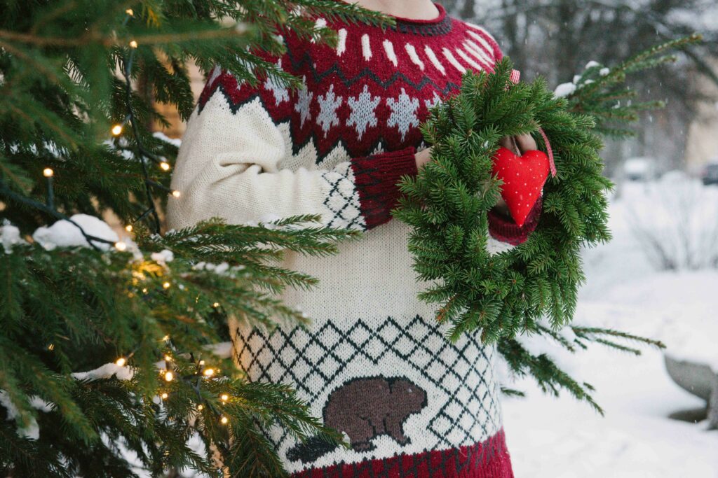 Nainen pitää joulukranssia kädessään joulukuusen vieressä.