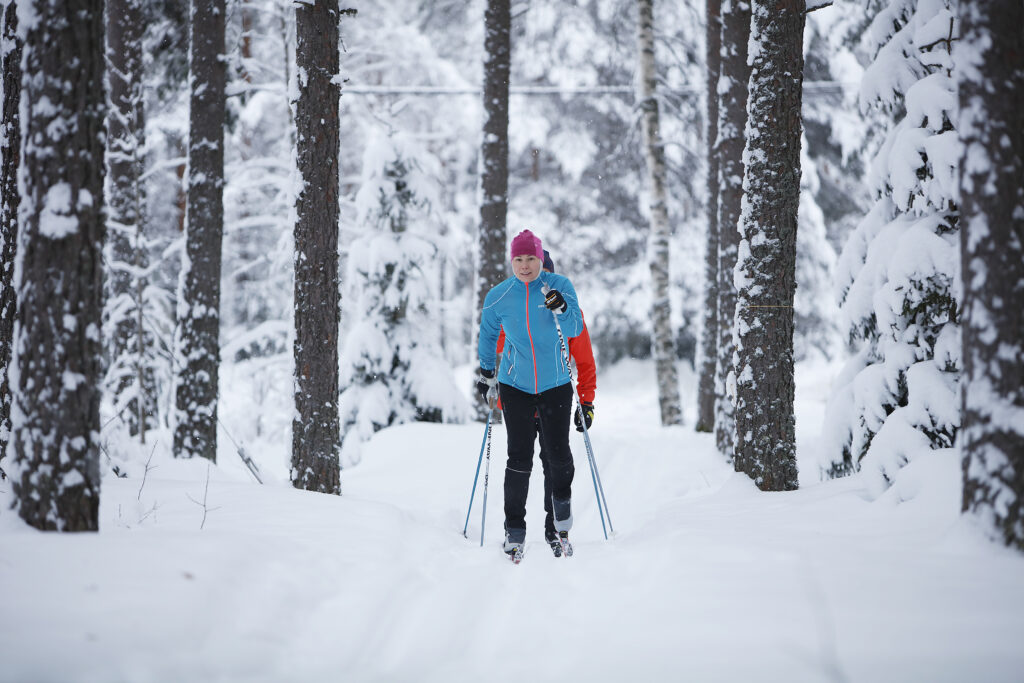 Hiihtäjä tulee kohti kameraa, taustalla talvinen metsä.