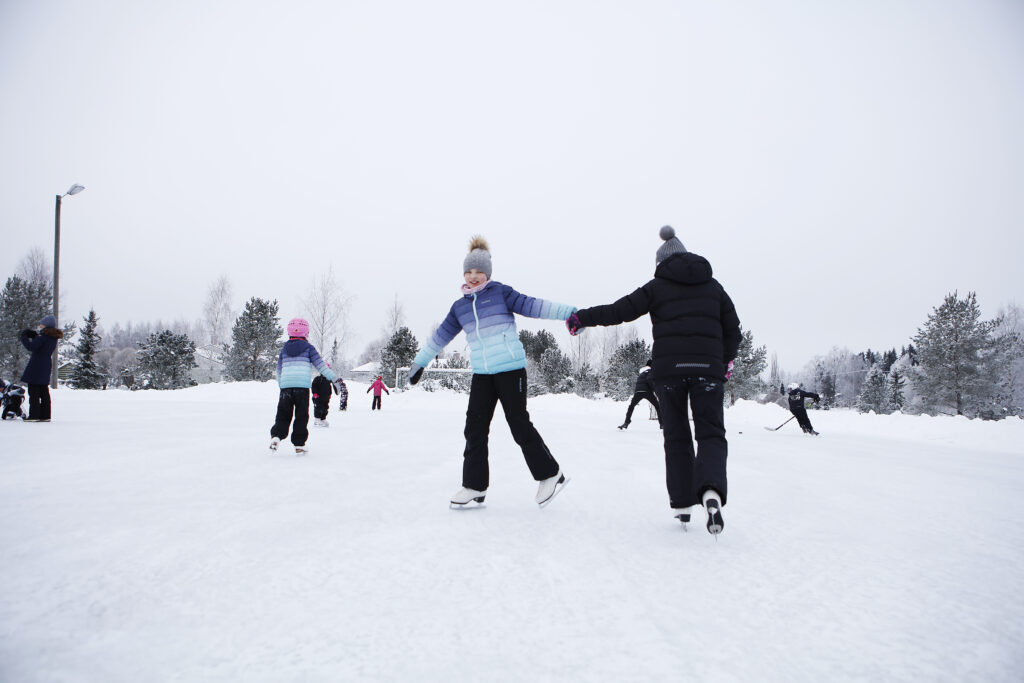 Luistelijat pyörimässä ympäri jäällä, toisiana kädestä pitäen.